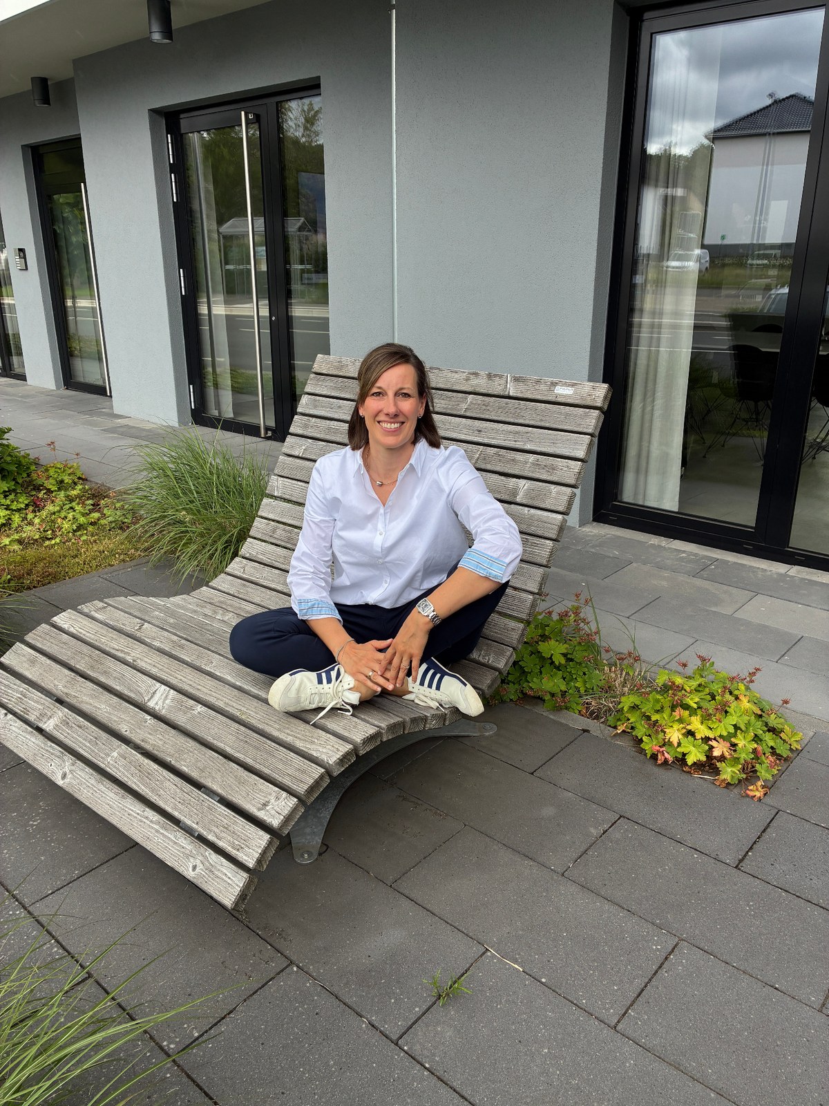 Sandra Pape sitzt auf einer Holzliege im Außenbereich.